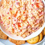 Pimento cheese in a bowl surrounded by round crackers.
