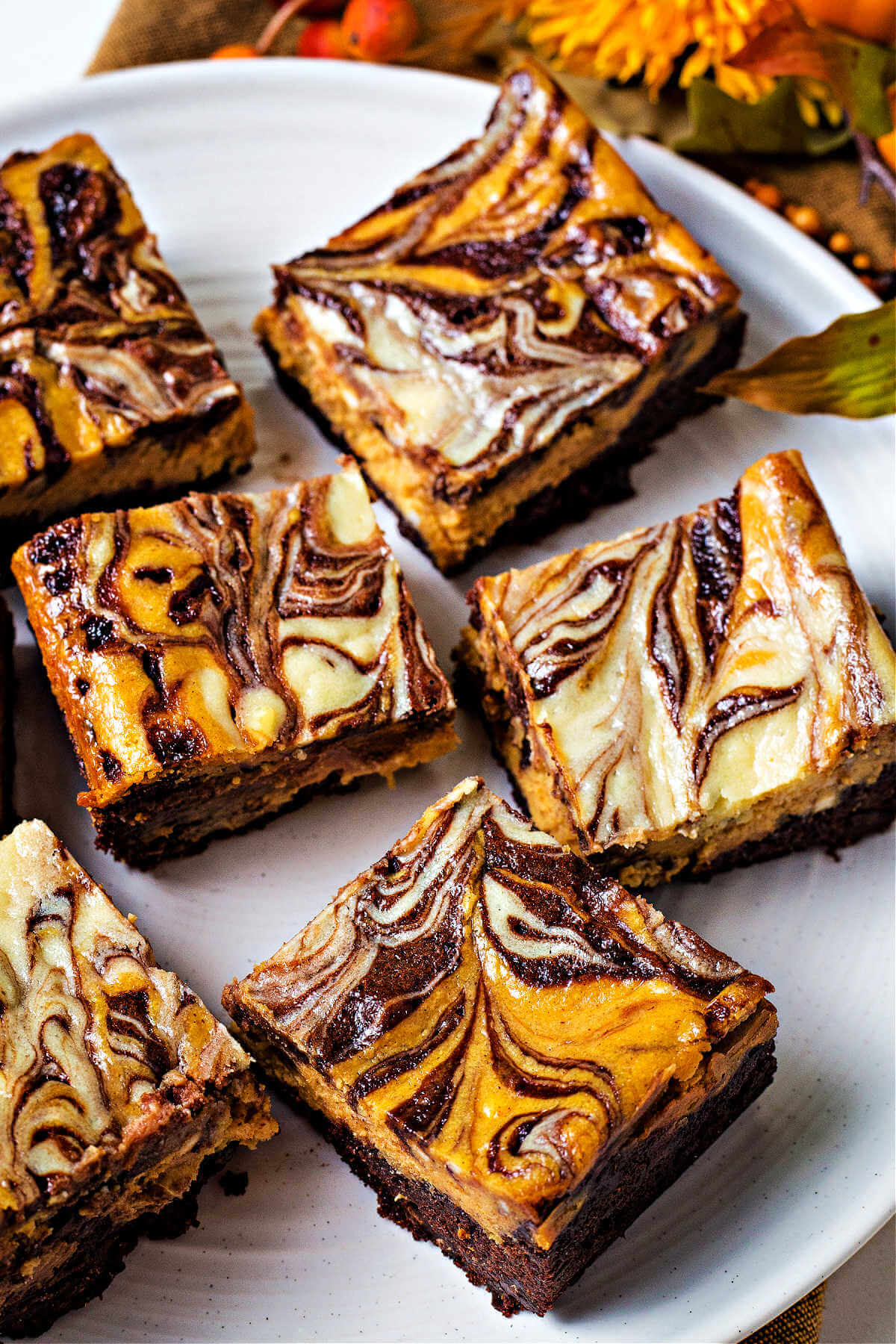 a plate of pumpkin cheesecake brownies with fall decorations in the background.