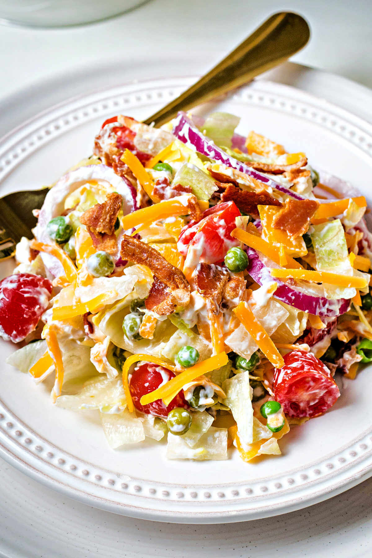 a serving of a tossed 7 layer salad on a plate with a gold fork.