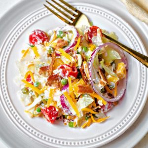 a serving of a tossed 7 layer salad on a plate with a gold fork.