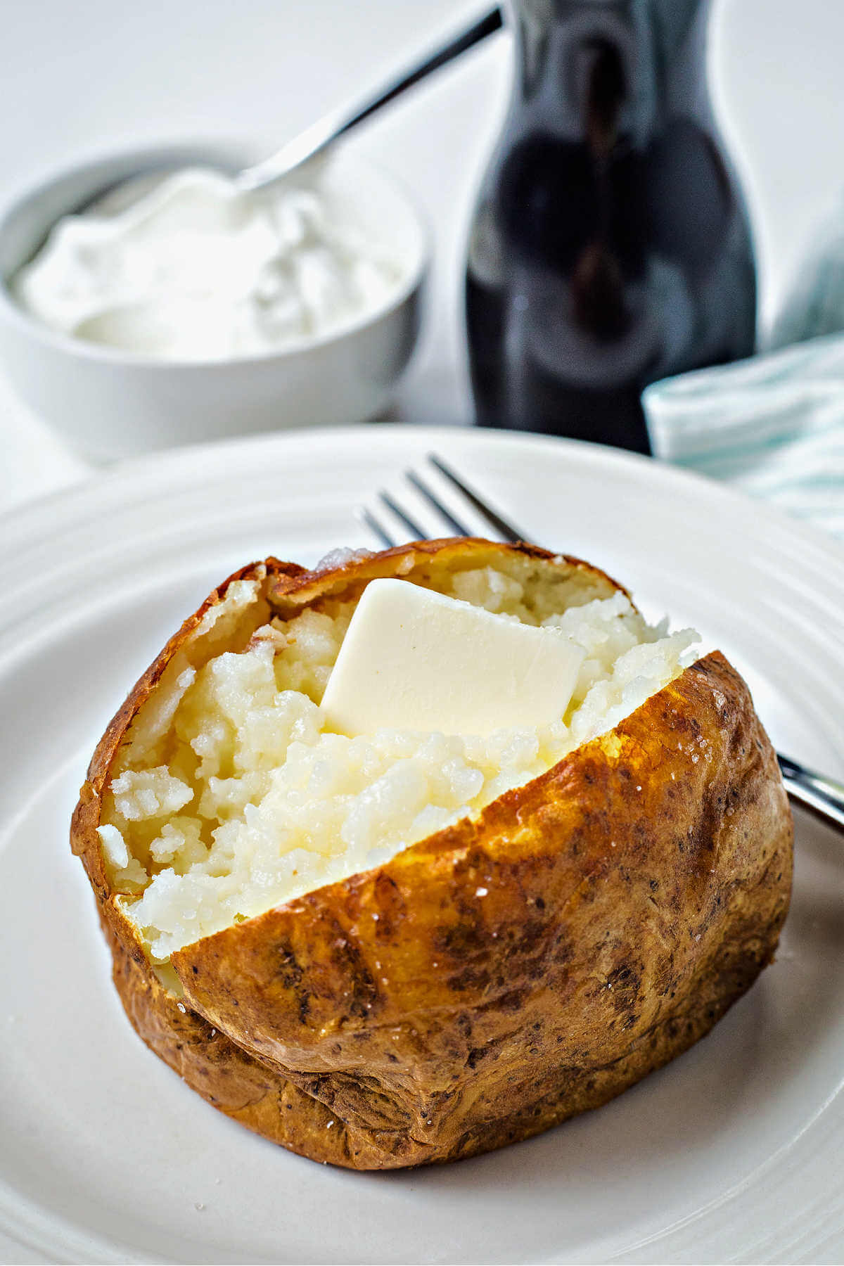 an air fryer baked potato topped with butter on a white plate on a table.