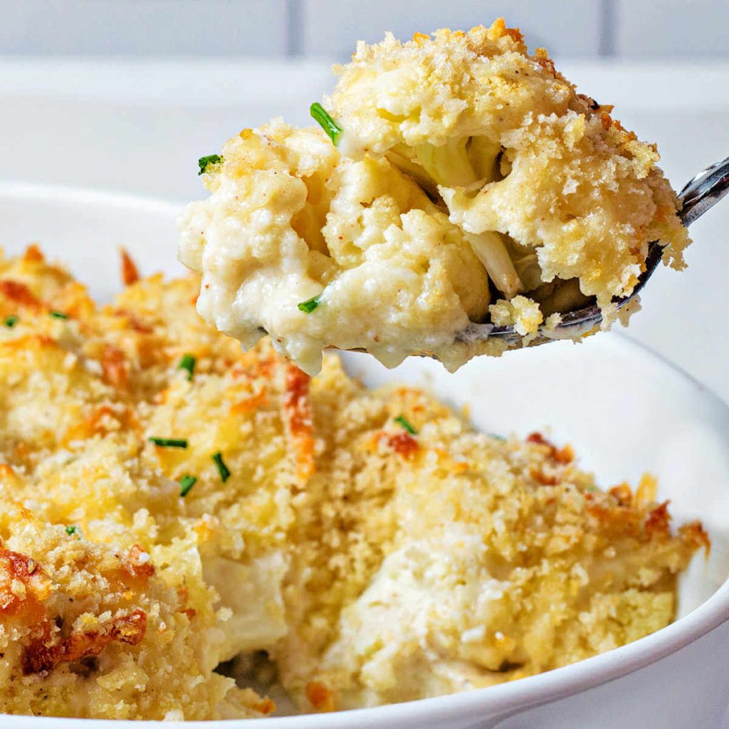 a serving spoon lifting out a spoonful of cauliflower gratin from a casserole dish.