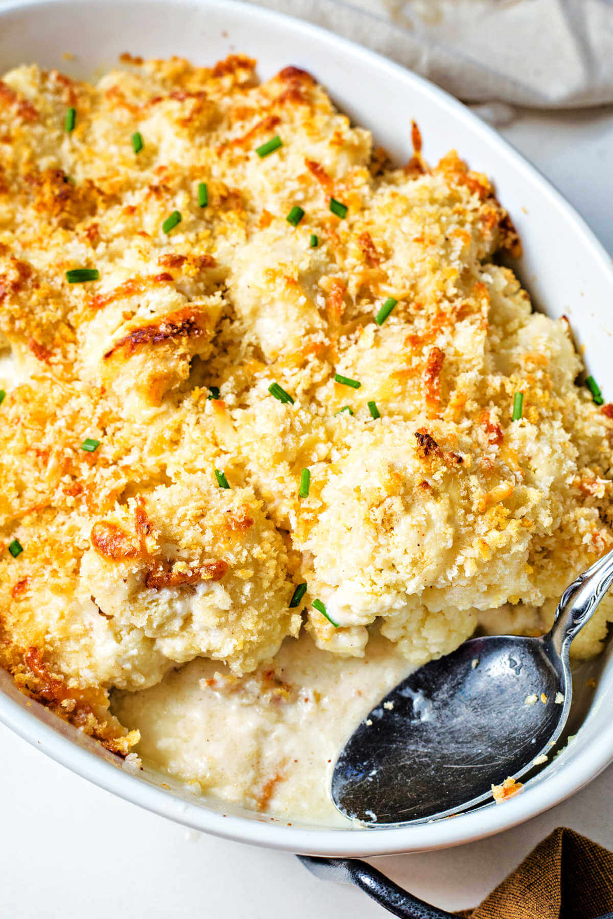 cauliflower gratin in a baking dish with a spoon and a serving missing.
