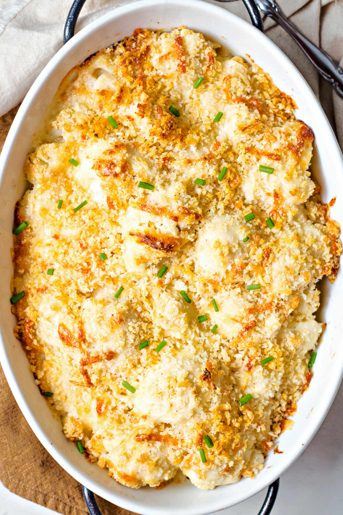cauliflower gratin with toasted breadcrumbs and garnished with chopped chives in a baking dish.