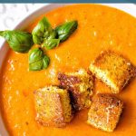 Creamy Tomato Soup garnished with fresh basil and parmesan cornbread croutons in a bowl.