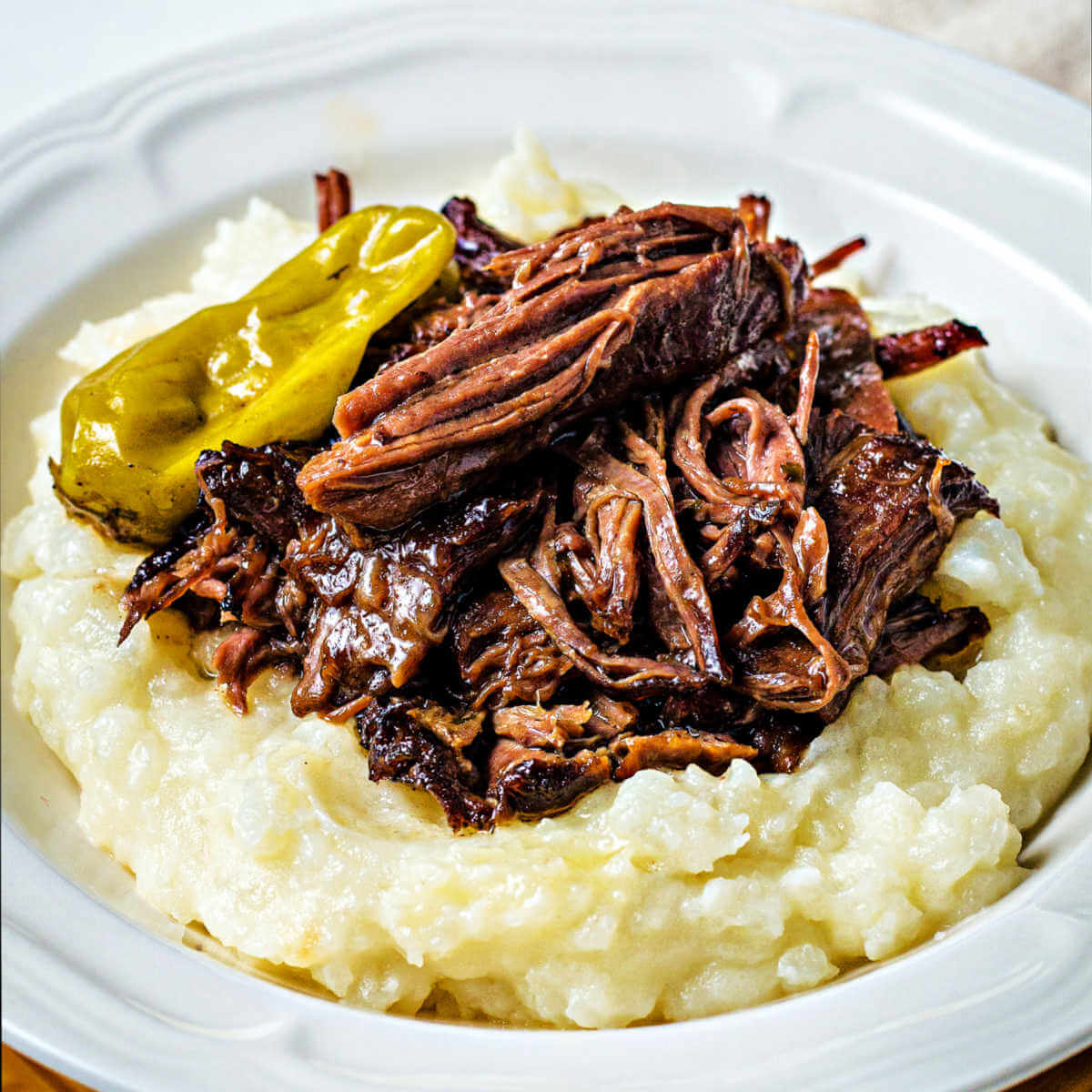 shredded Mississippi pot roast piled on top of a mound of mashed potatoes.