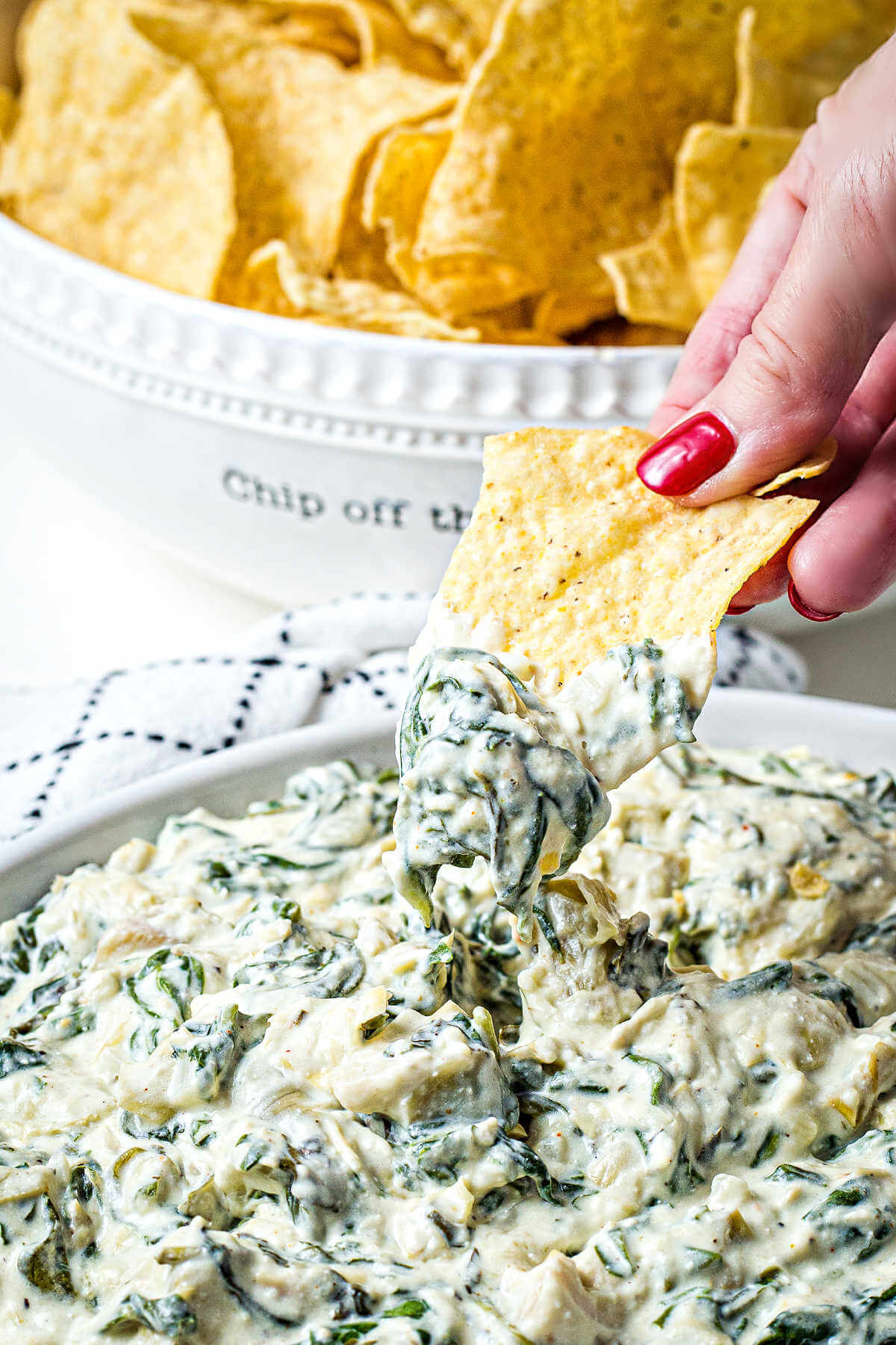 dipping a tortilla chip into a bowl of slow cooker spinach artichoke dip.
