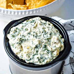 slow cooker spinach artichoke dip in a small crock pot on a table.