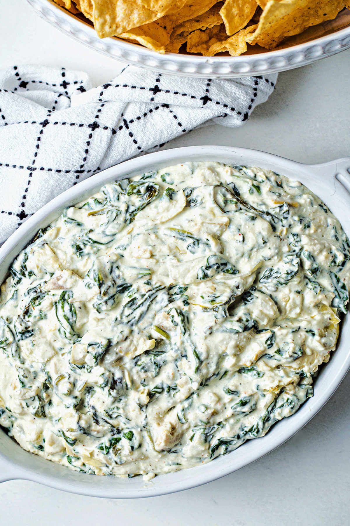 hot spinach artichoke dip in a baking dish on a table with a bowl of chips.