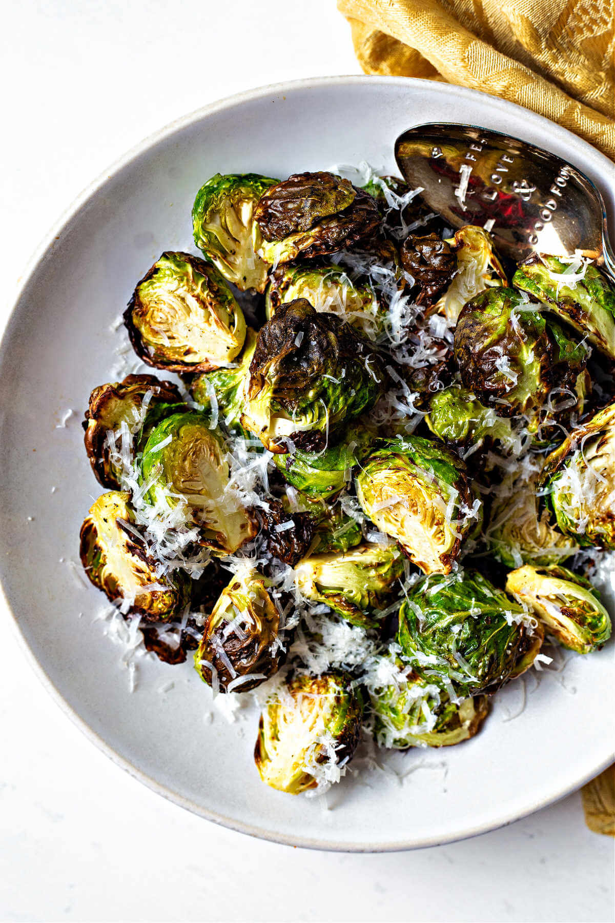 crispy air fryer brussels sprouts in a white bowl with freshly grated parmesan cheese sprinkled on top.