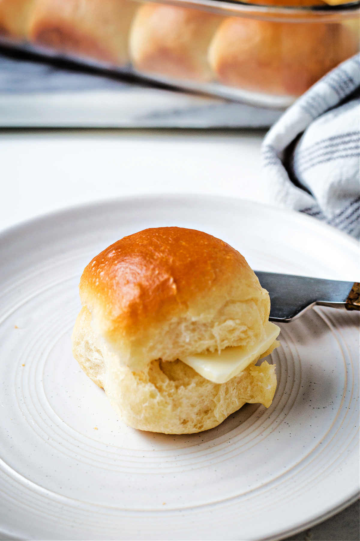 a dinner roll with a knife and butter on a plate.
