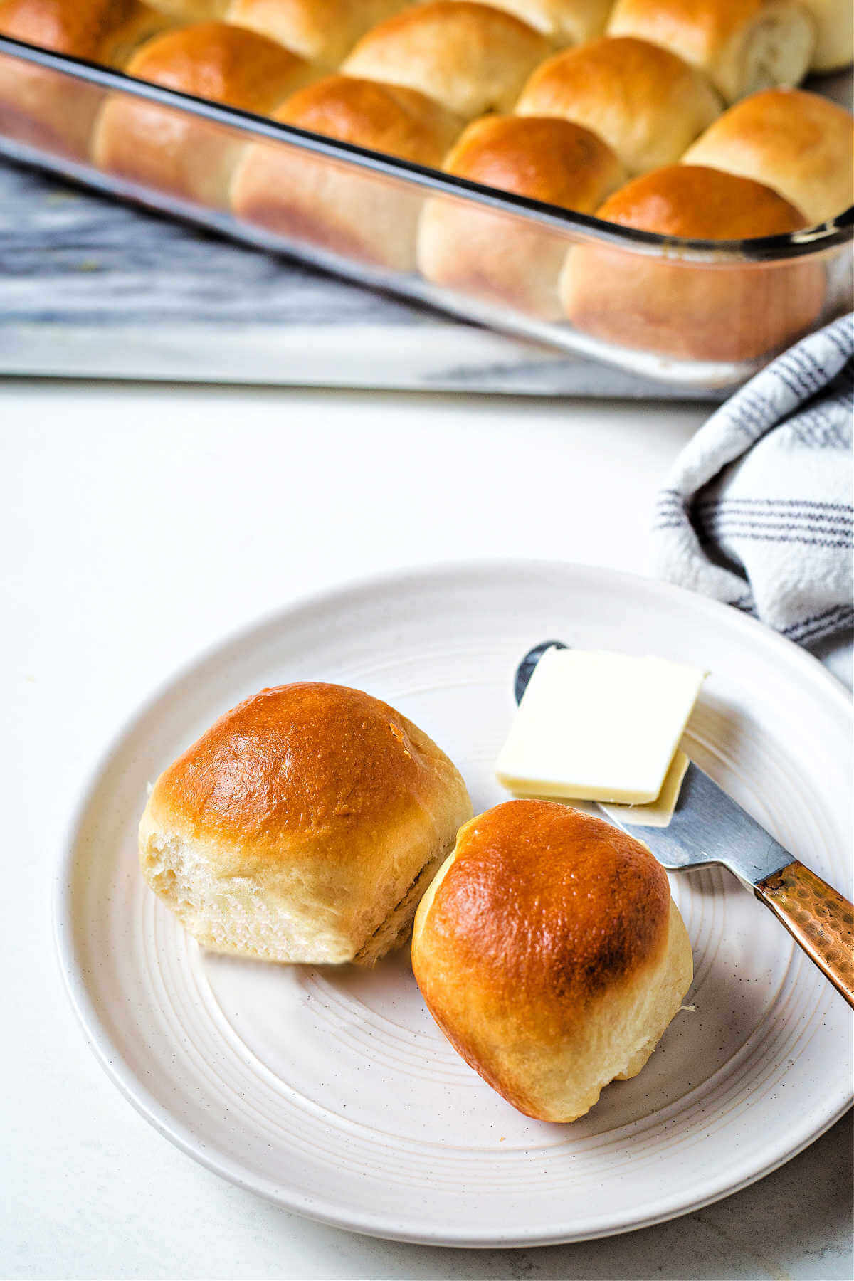 two dinner rolls with a knife and butter on a plate.