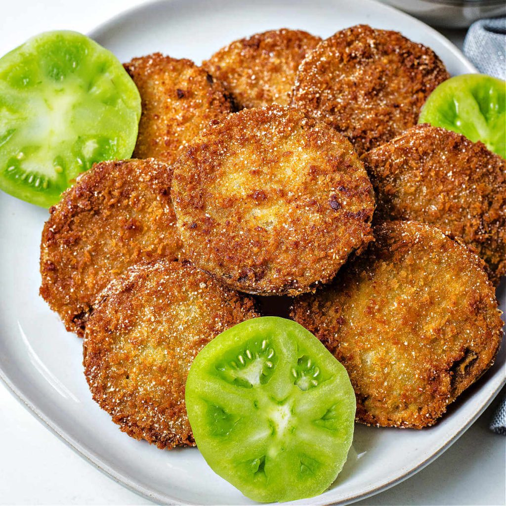 sliced of fried green tomatoes on a plate garnished with raw green tomato slices.