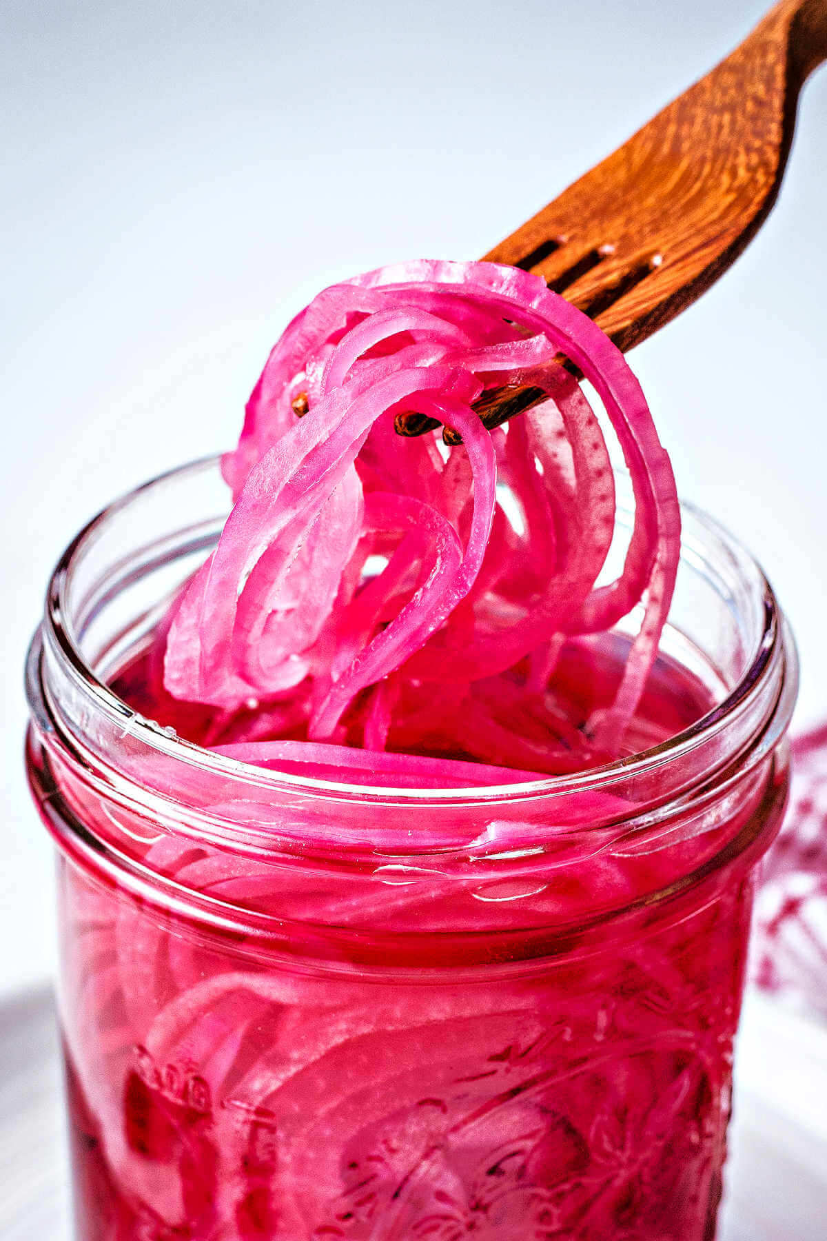 a wooden fork lifting out pickled red onions from a jar.