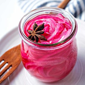 a jar of pickled red onions with a star anise floating on top.