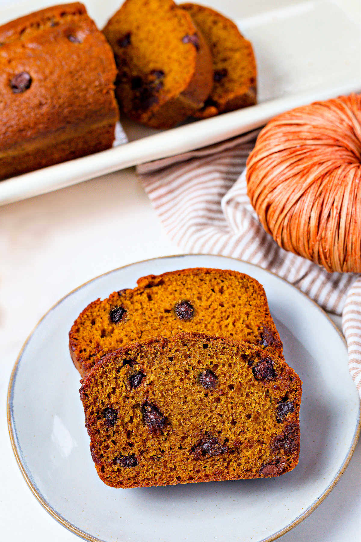 two slices of pumpkin bread with chocolate chips on a plate with the remaining loaf in the background.