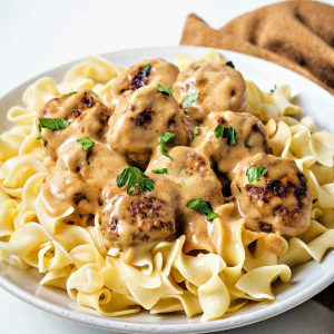 Swedish meatballs and gravy over a beg of noodles in a white bowl.