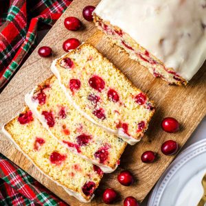 cranberry orange bread on a wooden tray with cranberries scattered around.