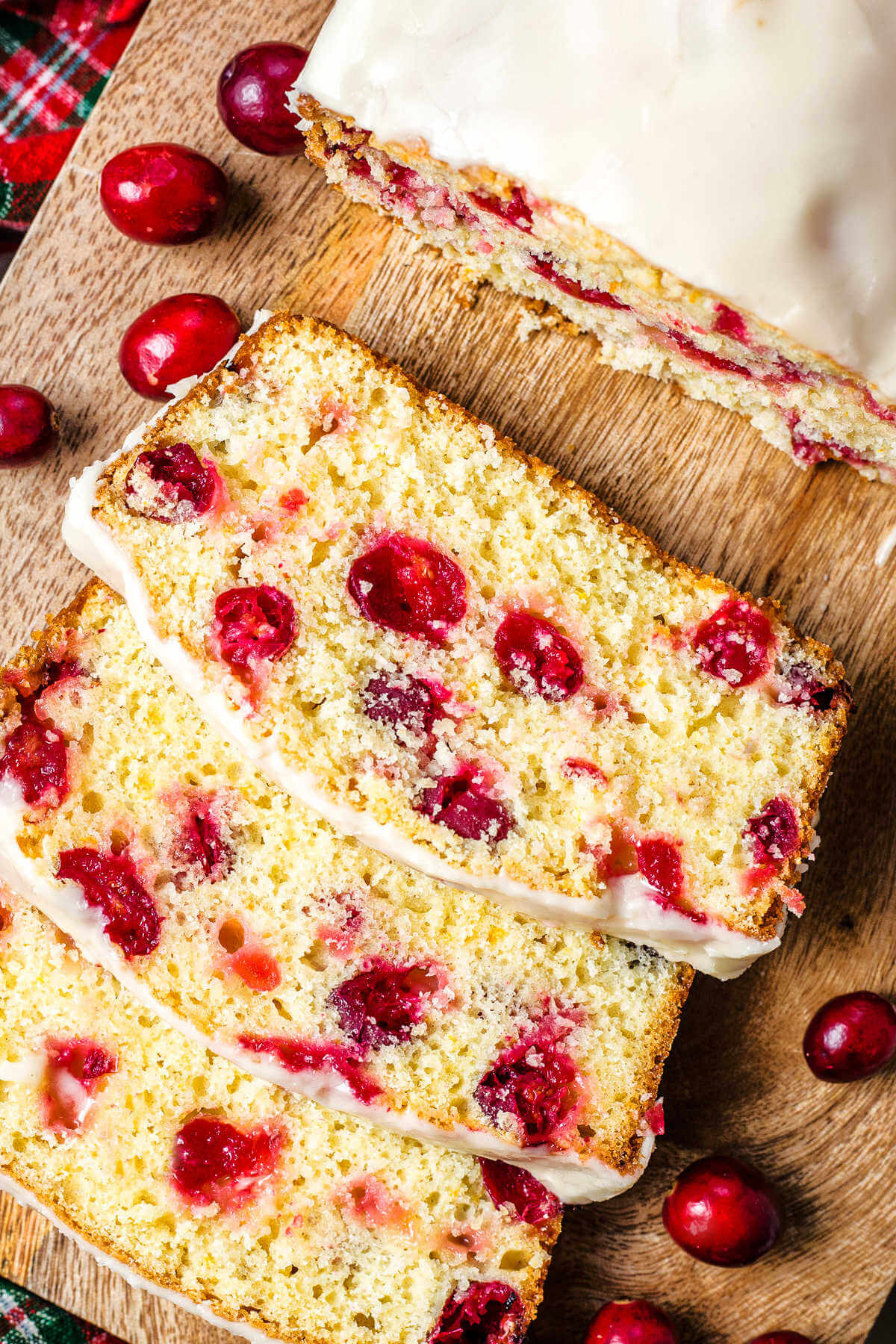 three slices of cranberry orange bread on a wooden tray with cranberreis.