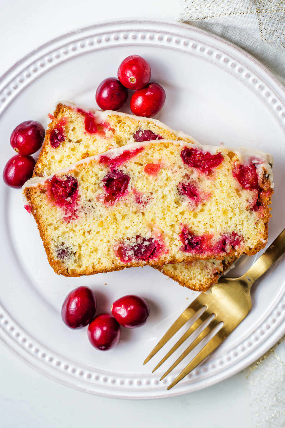 two slices of cranberry orange bread on a plate with a gold fork.