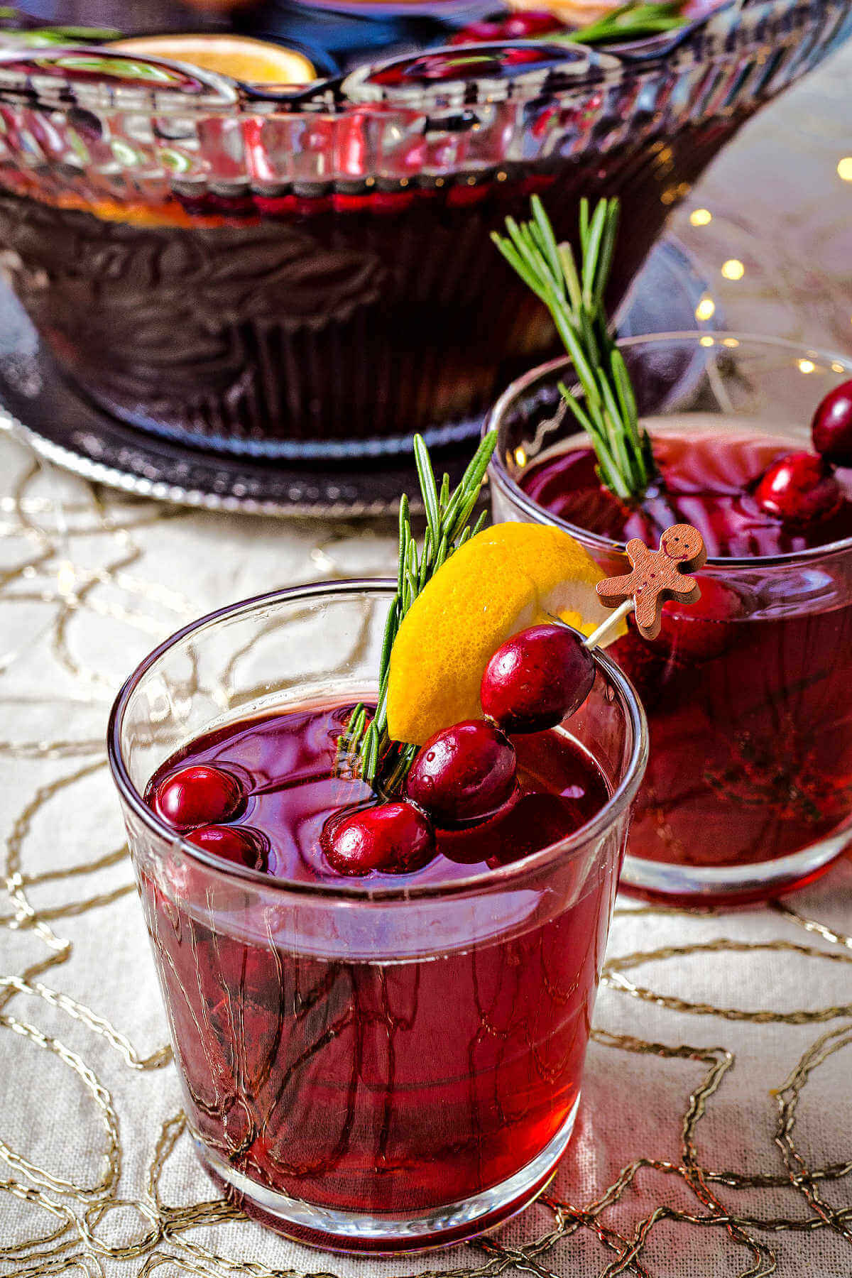 a glass of Cranberry White Grape Punch garnished with cranberries, an orange slice, and rosemary sprig on a table.