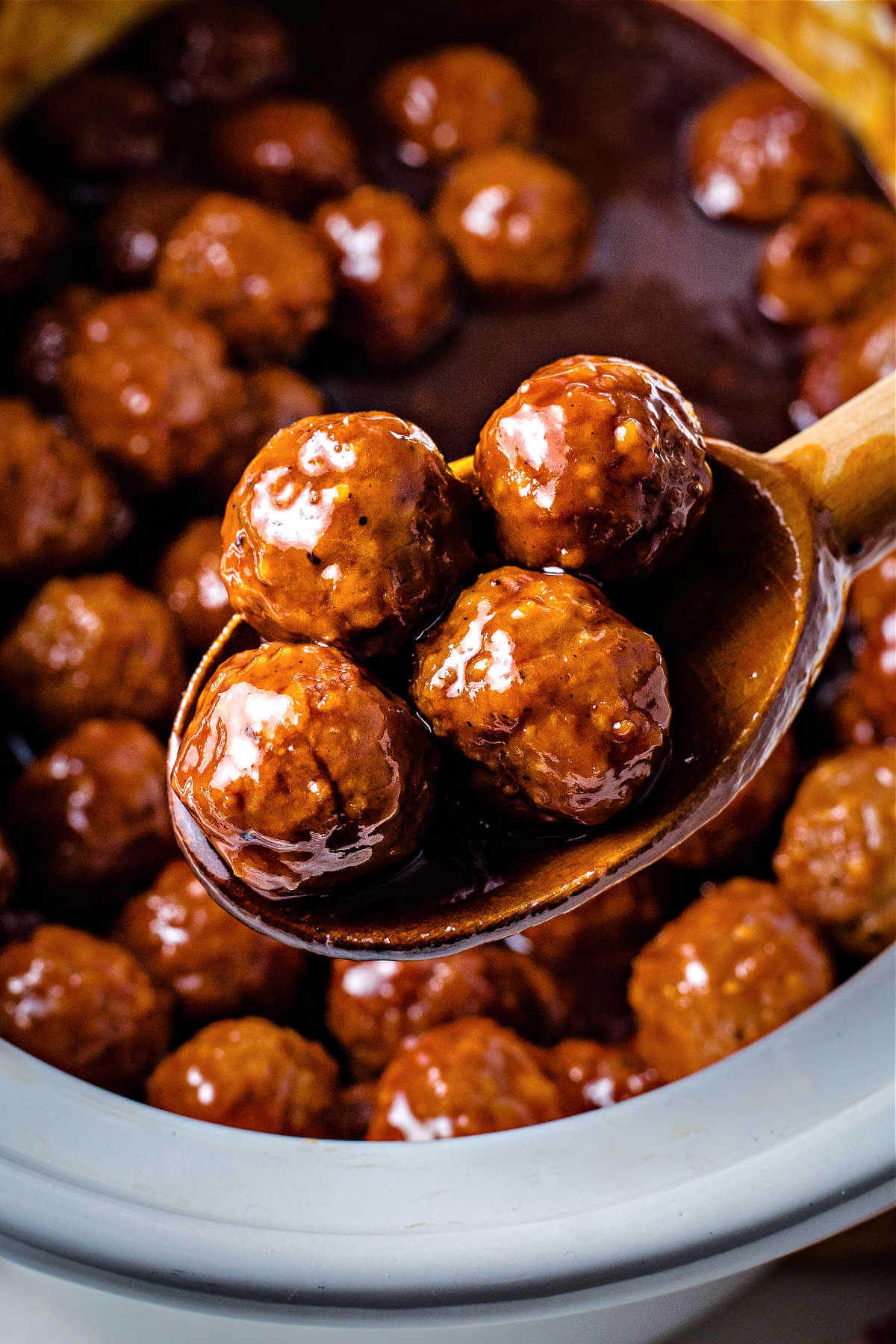a wooden spoon lifting grape jelly meatballs out of a crockpot.