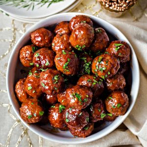 a bowl of grape jelly meatballs garnished with chopped parsley on a table.