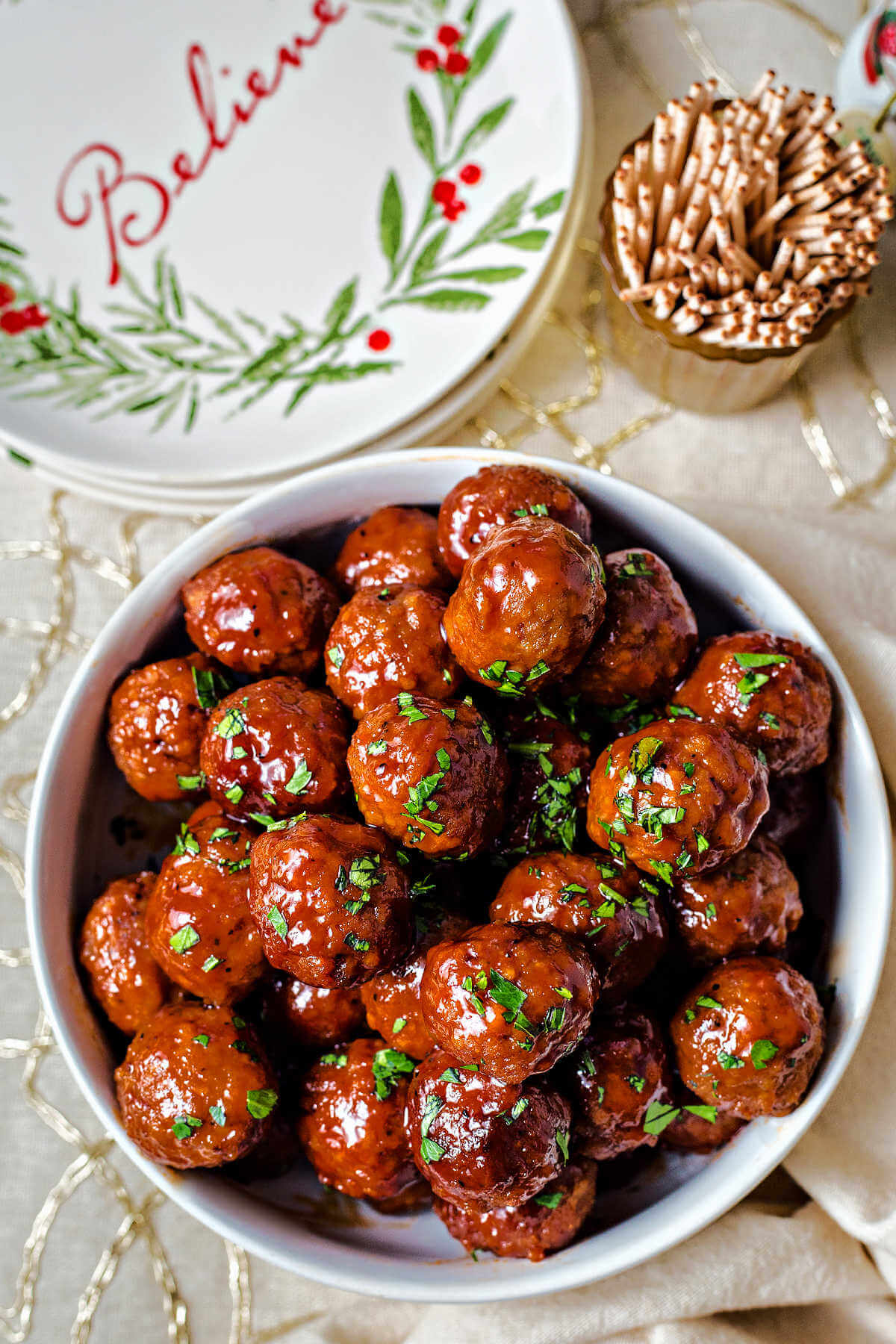 a bowl of grape jelly meatballs garnished with chopped parsley on a table with appetizer plates.