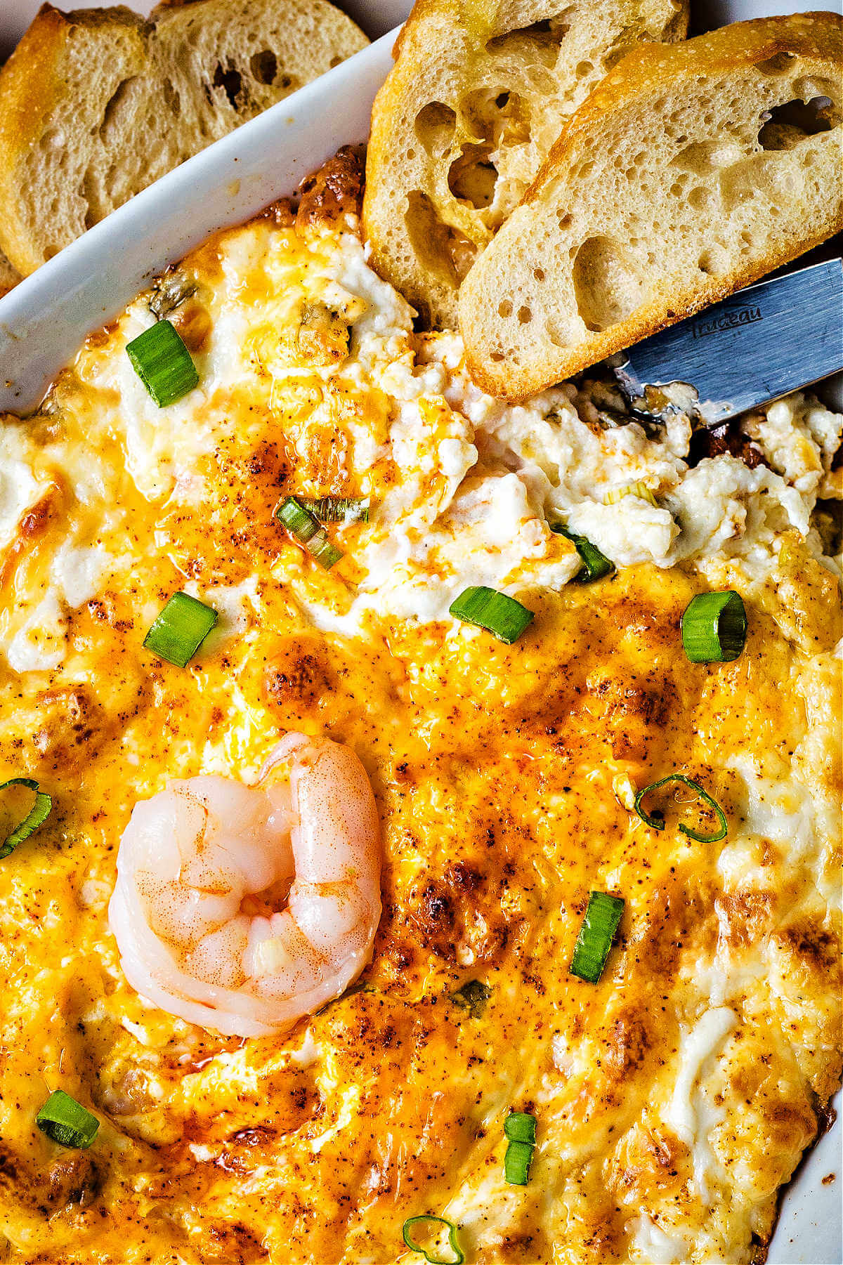shrimp dip with a shrimp on top as garnish and a baguette dipping into the dish.