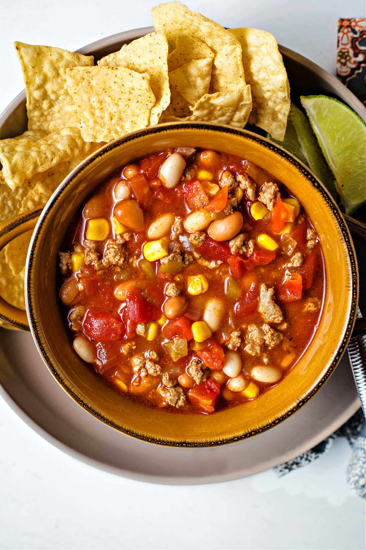 a bowl of easy taco soup on a plate with tortilla chips and lime slices.