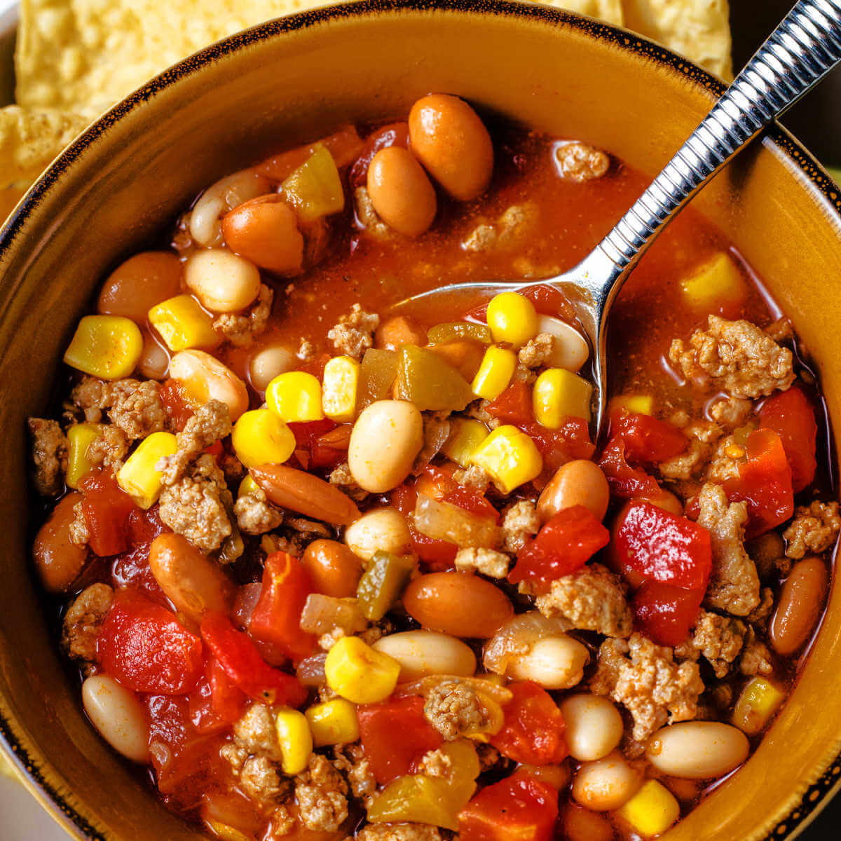 a bowl of taco soup with a spoon inserted in the bowl on a table.