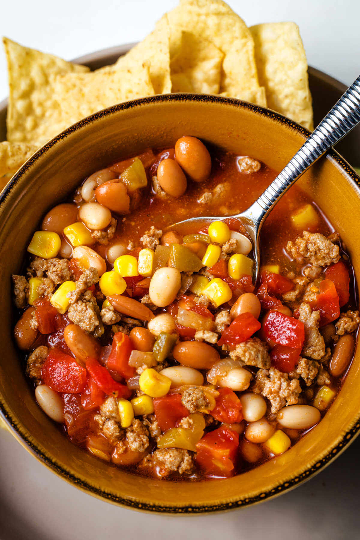 a bowl of taco soup with a spoon and a plate of tortilla chips on a table.