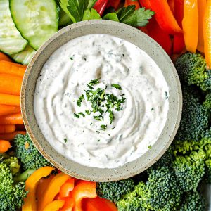 a bowl of vegetable dip garnished with chopped parsley on a platter with vegetables for dipping.