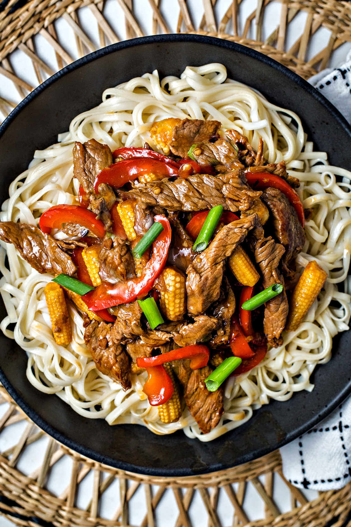 Korean Beef Stir Fry served over lo mein noodles in a bowl sitting on a rattan placement.