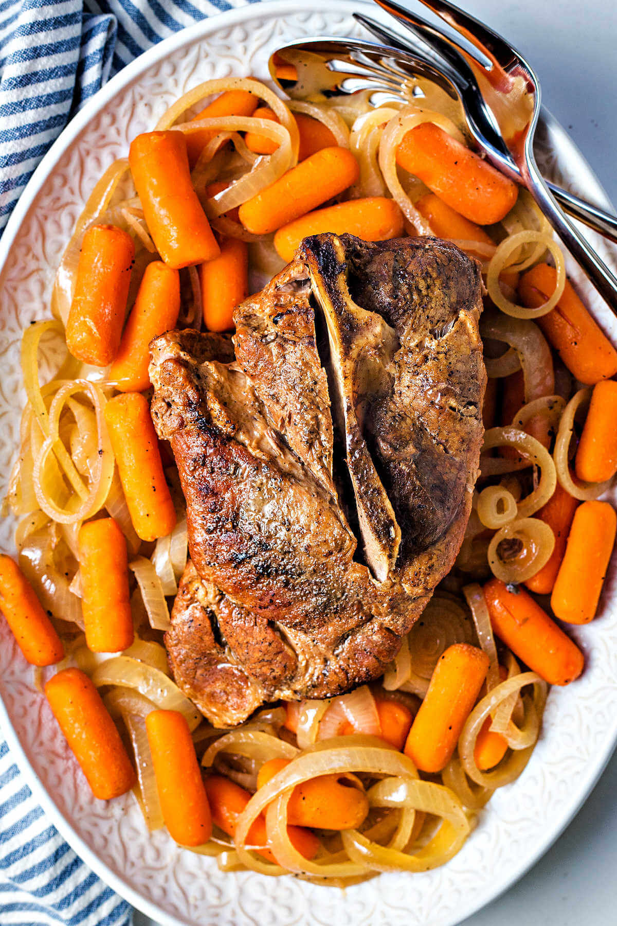 slow cooker pork roast on a platter surrounded by carrots and onions.