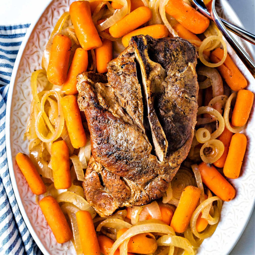 slow cooker pork roast on a platter surrounded by carrots and onions.