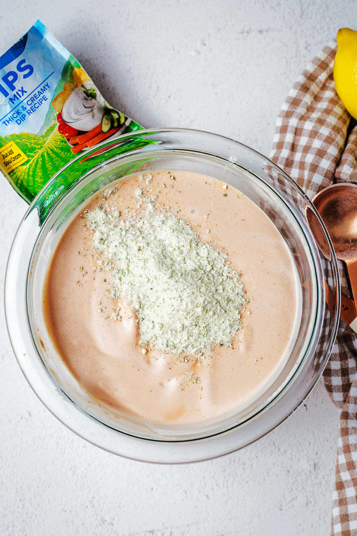 dry ranch seasoning mix sprinkled into a bowl with BBQ ranch dressing ingredients.