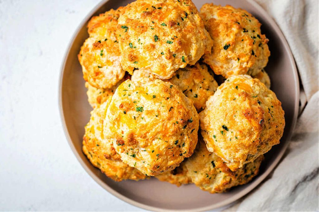 a plate of cheddar bay biscuits on a table with a linen napkin tucked beside the plate.