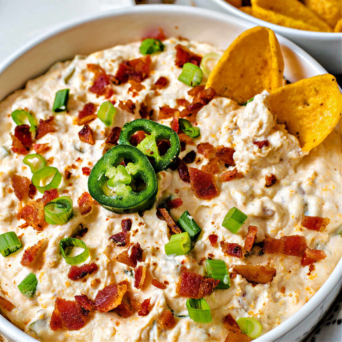 jalapeno popper cheese dip in a bowl garnished with bacon and green onions.