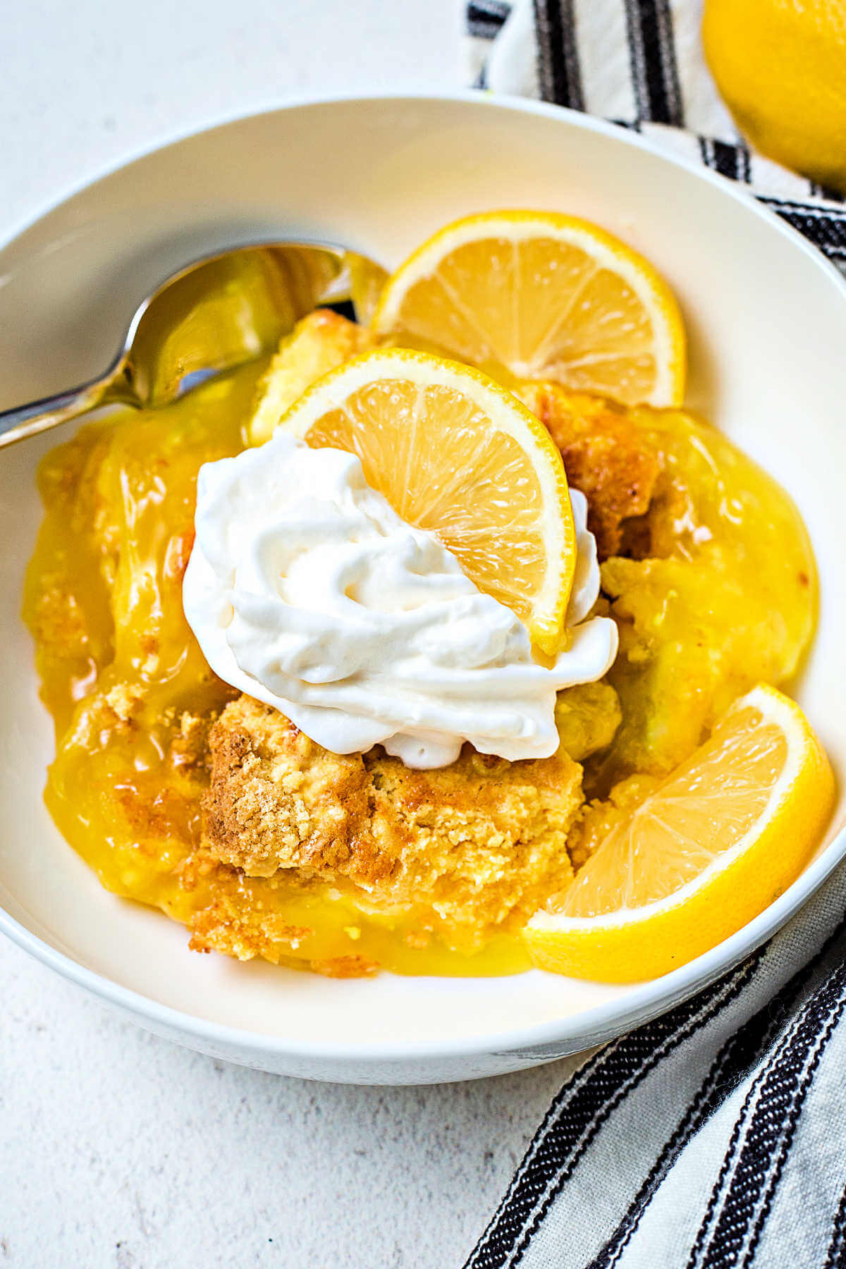 a serving of lemon dump cake topped with whipped cream and garnished with fresh lemon slices.