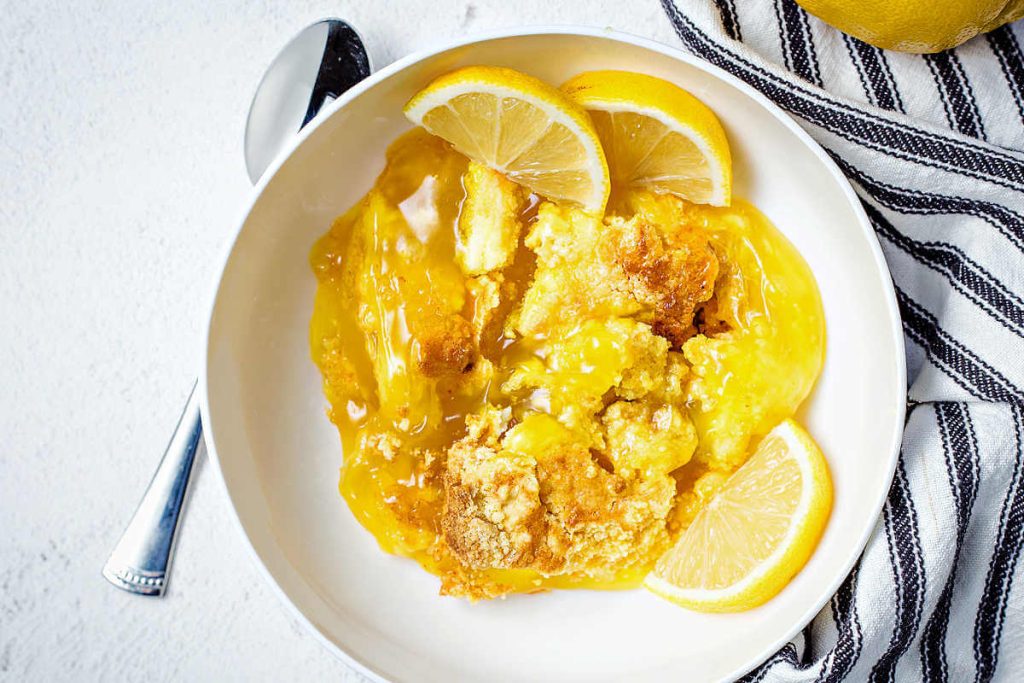 a serving of lemon dump cake garnished with fresh lemons on a table with a striped napkin.