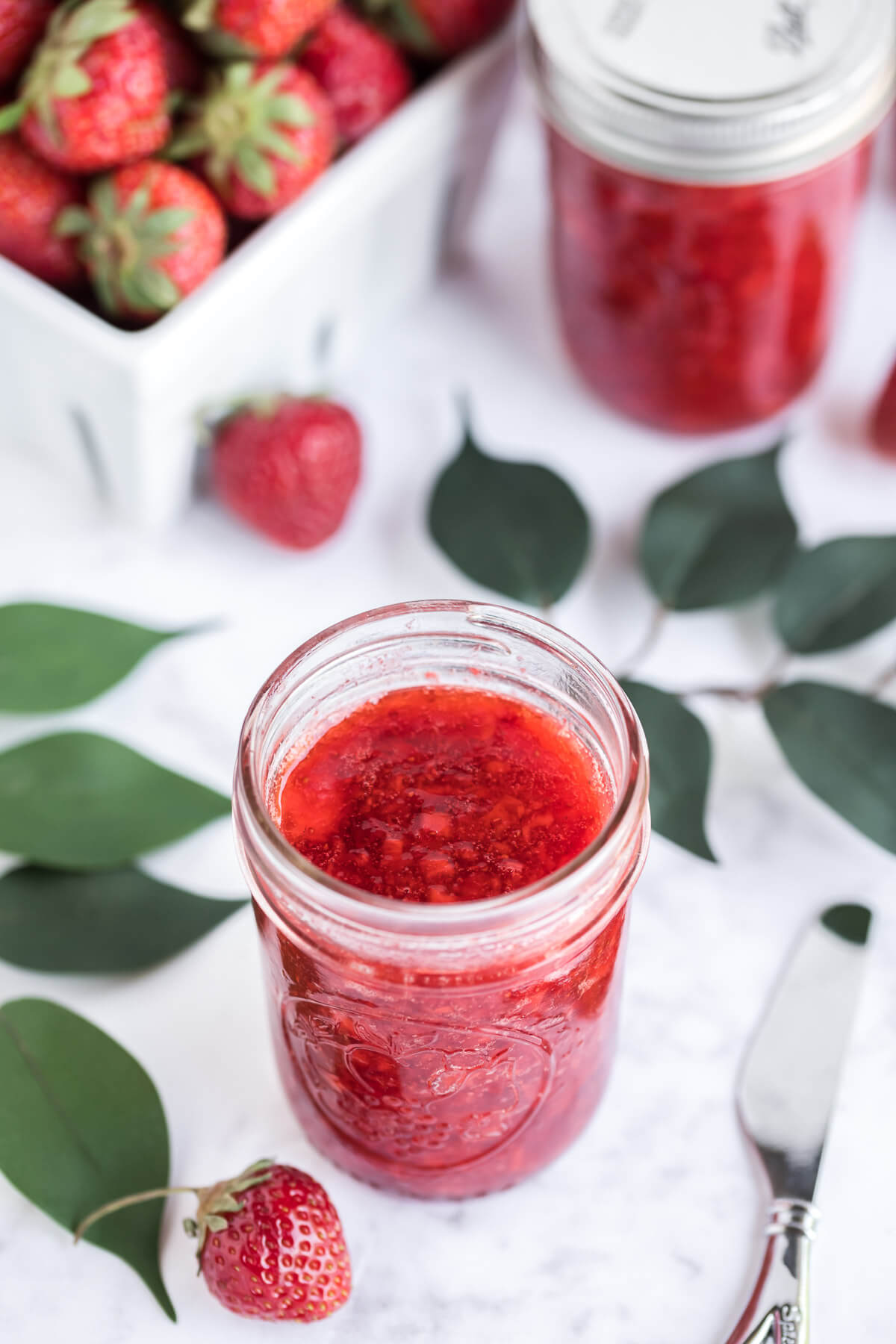 strawberry jam in glass jars sitting on a table.