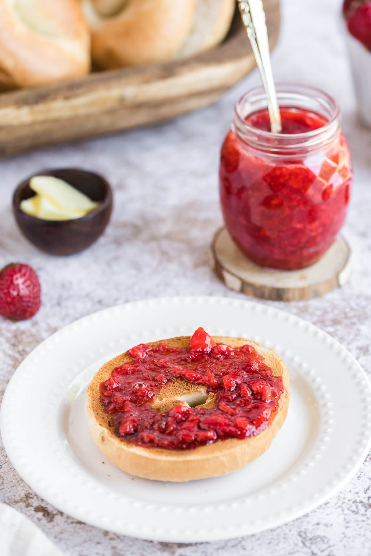 strawberry jam spread on a toasted bagel on a white plate.