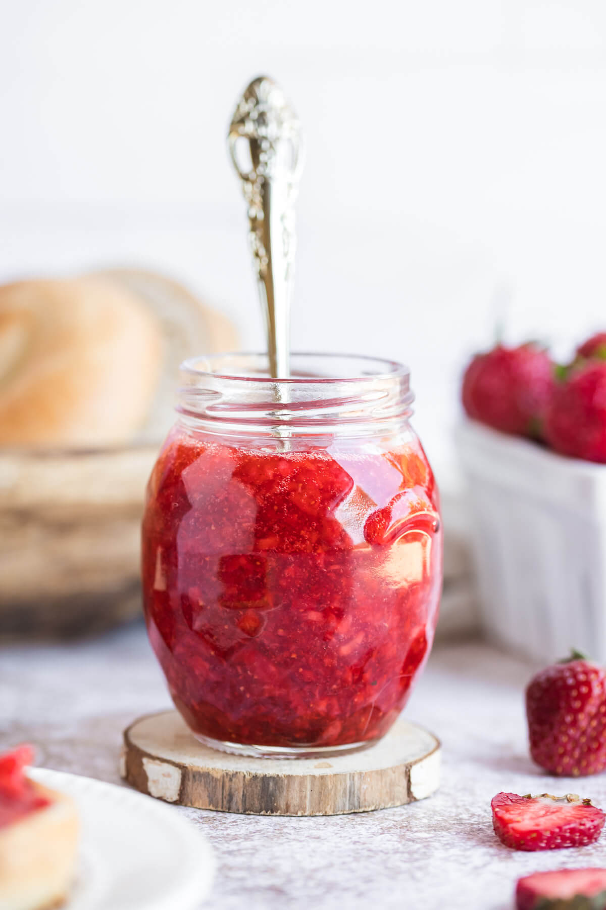 strawberry freezer jam in a glass jar with a spoon on a table.