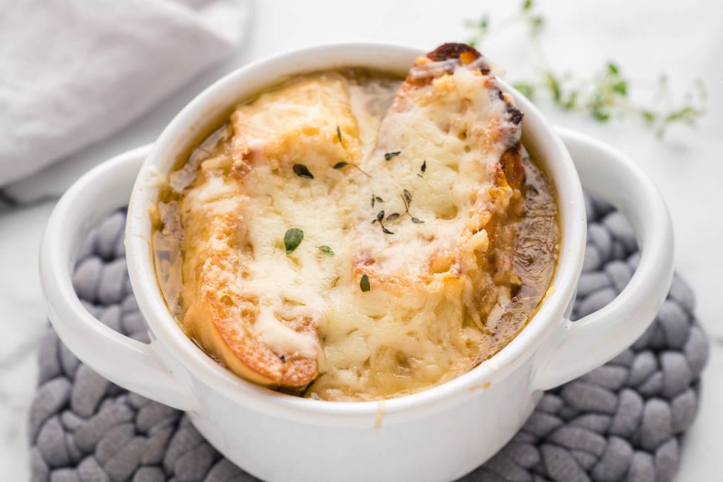 Gruyere cheese toast floating on top of French onion soup in a white bowl.