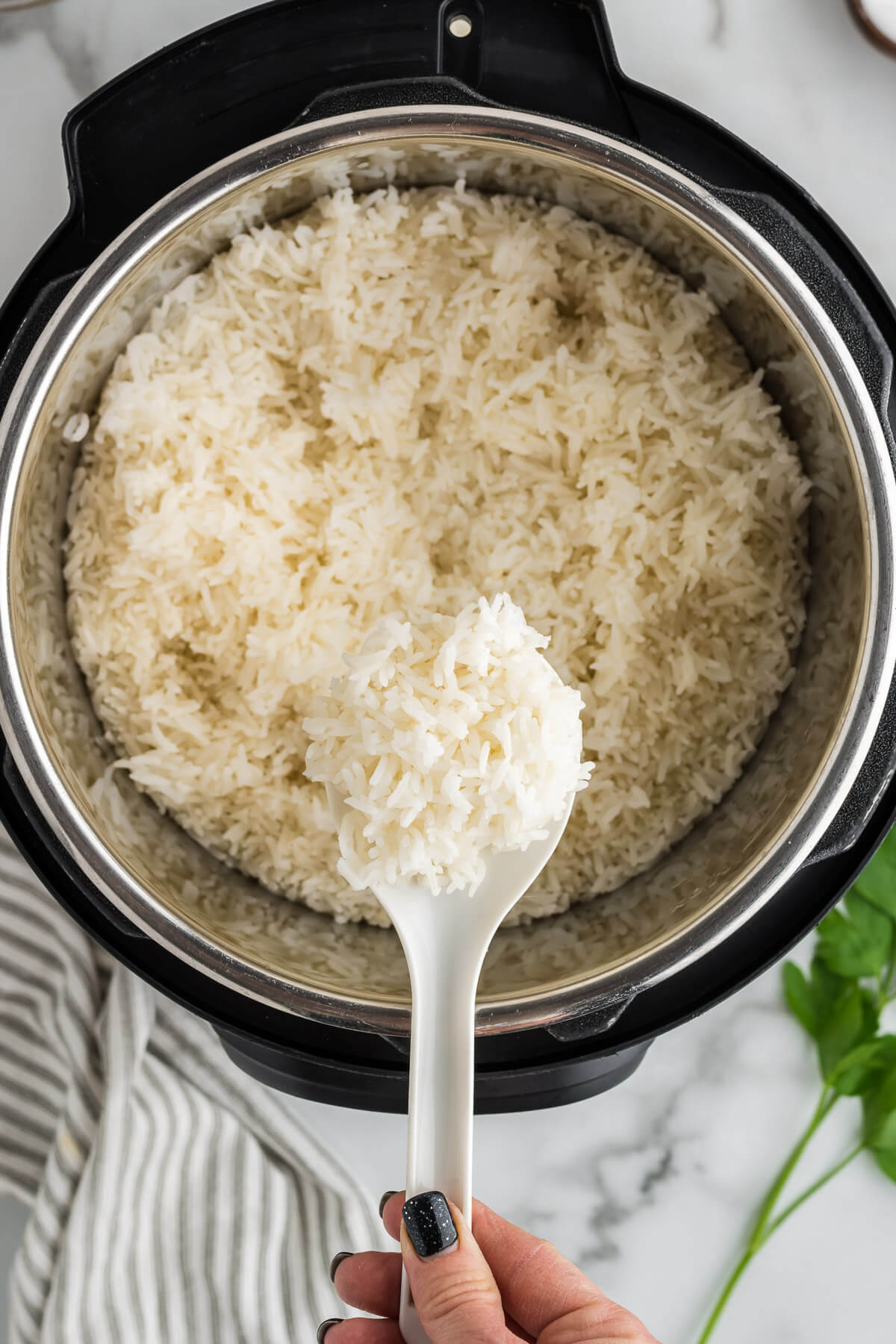 a hand holding a spoon of rice over an open instant pot.