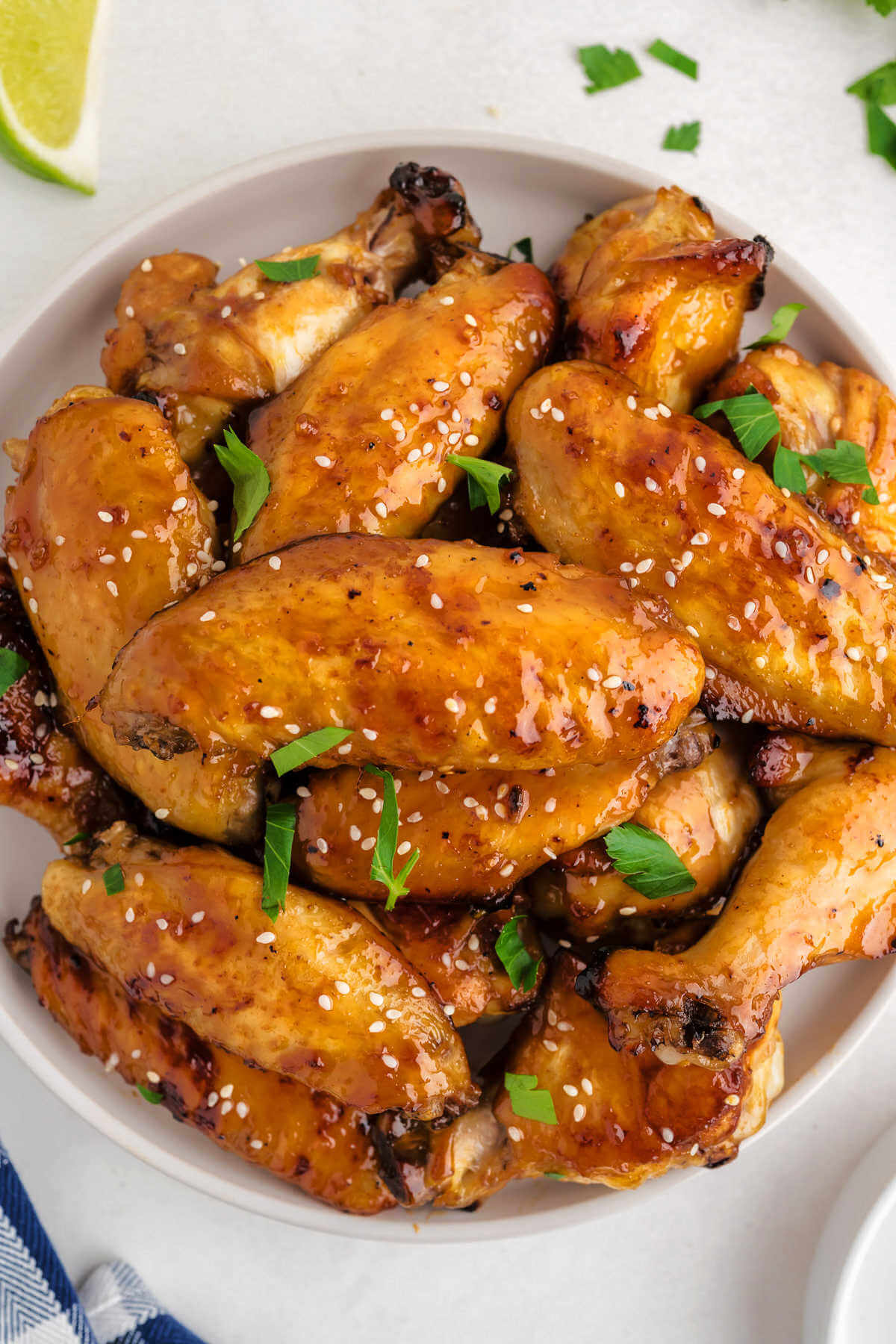 sticky baked chicken wings piled on a white plate garnished with sesame seeds and cilantro.