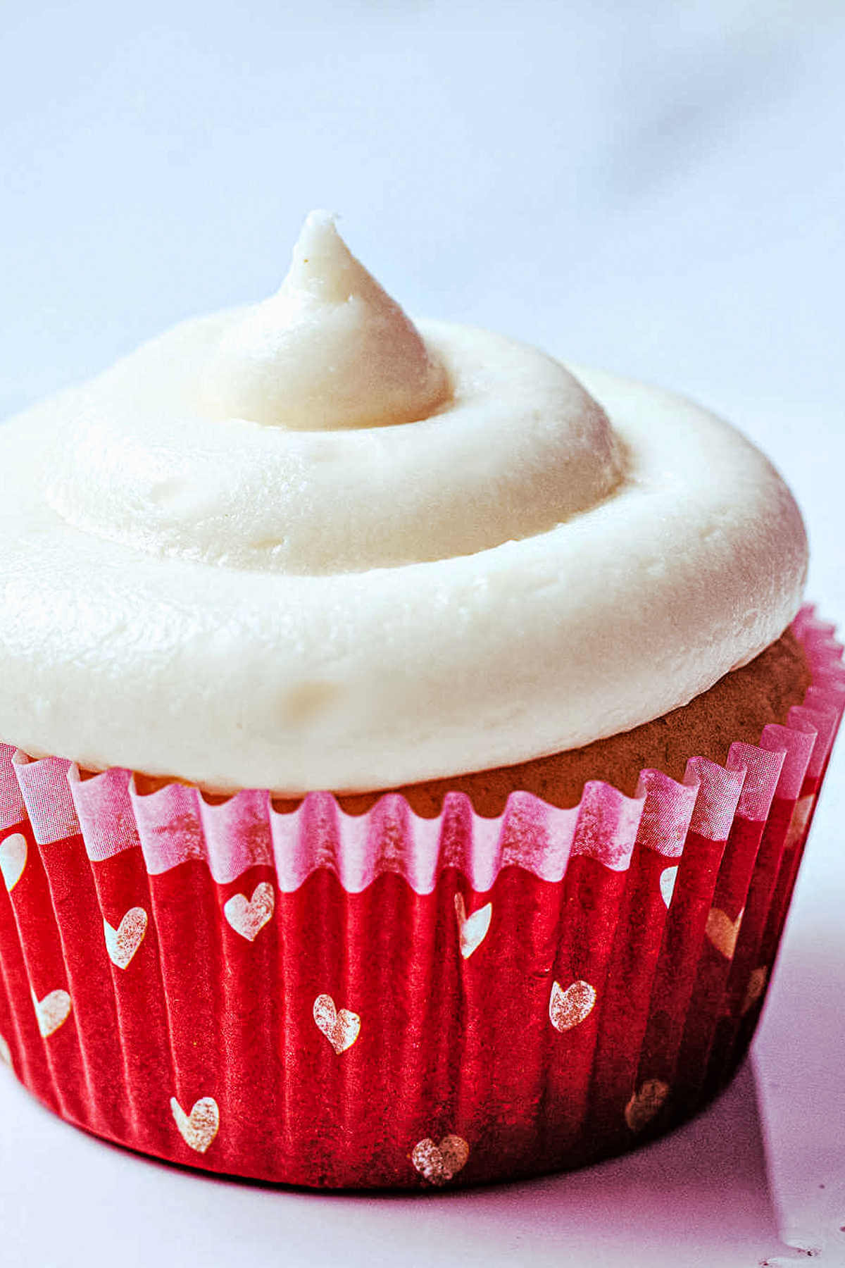 a vanilla cupcake with sour cream frosting in a heart decorated paper liner.