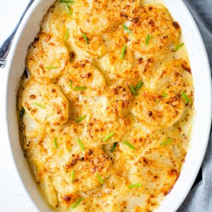 browned and cheesy instant pot scalloped potatoes garnished with fresh chives in a white baking dish.