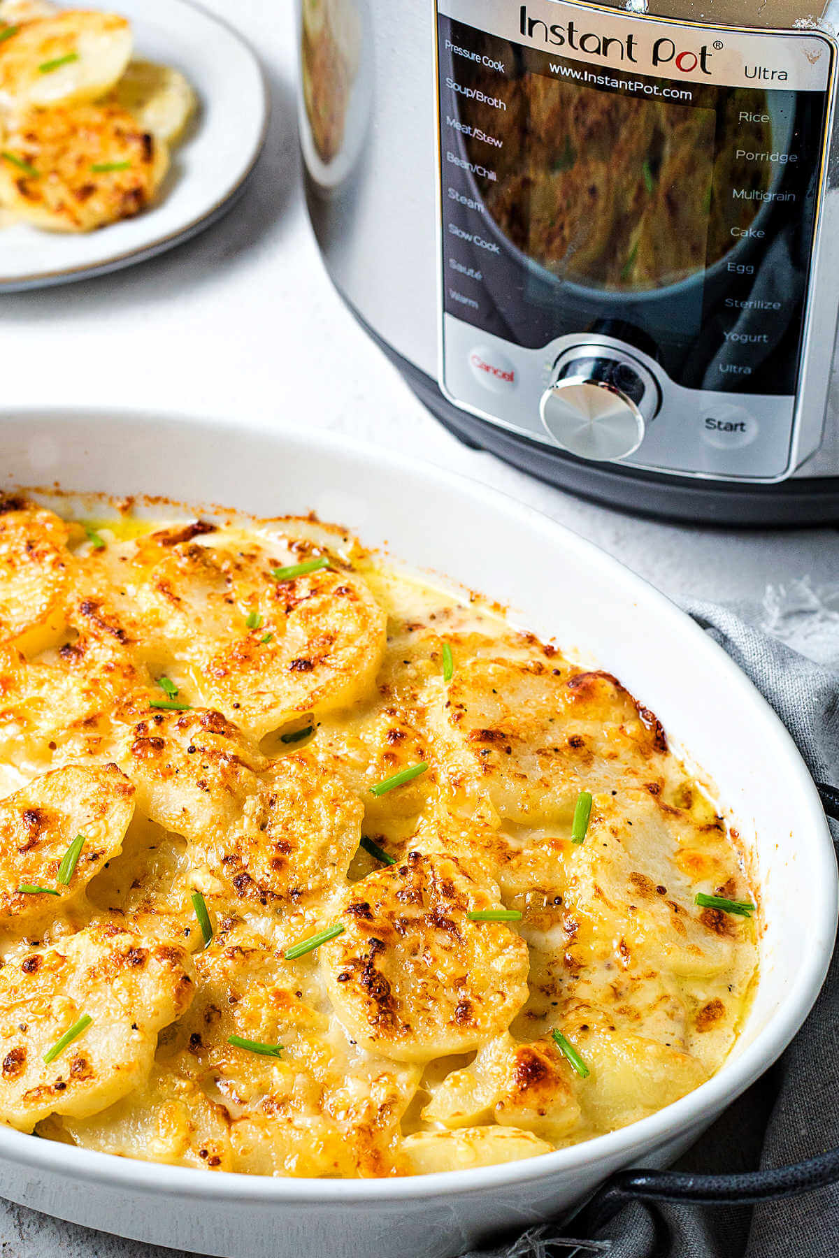 a baking dish with broiled scalloped potatoes on a table with an instant pot in the background.